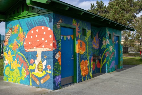 A revitalized public restroom covered in colorful murals with redcap mushrooms, brown beetles, green grass.