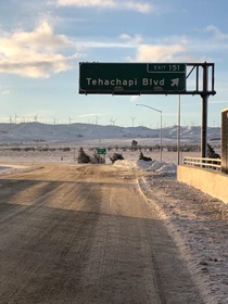 Windmills turn in the distance behind the Tehachapi Boulevard Exit 151 sign on State Route 58 as the highway reopens following heavy snow on December 15, 2021.