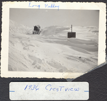 A black and white image of a truck driving over a completely snowed over road. Writing on the picture reads "Long Valley. 1936 Crestview."