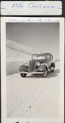 A black and white image of an old car driving on a snowy road in 1936. The writing on the image reads "1936 Crestview. Between Mammoth and June Lake."