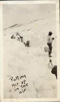 An undated black and white image of men shoveling snow with shovels on the highway. Writing on the picture reads "Putting her up in the air."